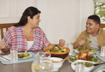 Mother and son sit at dinner table smiling as they eat a healthy meal.