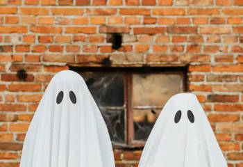 Two individuals in ghost costumes standing in front of a brick wall.