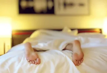 Image of a person's feet sticking out of the covers as they lay face down on a bed.