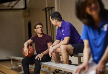 A Y associate sits on the bleachers and talks with a member holding a basketball.