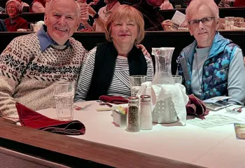 Three members sitting together at a table at the New Theater Restaurant. Other attendees are in the background.