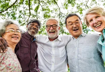 A group of five adults huddle around the camera and smile