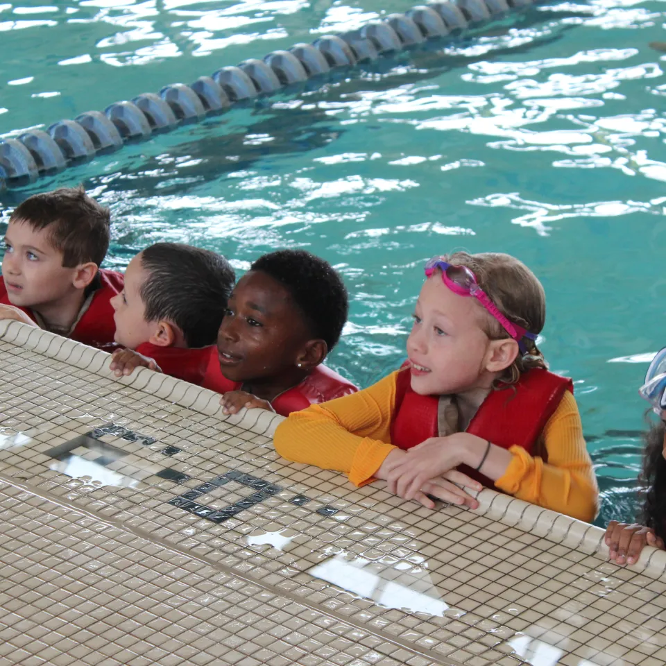 5 children smiling while resting on the edge of a Greater Kansas City YMCA swimming pool.