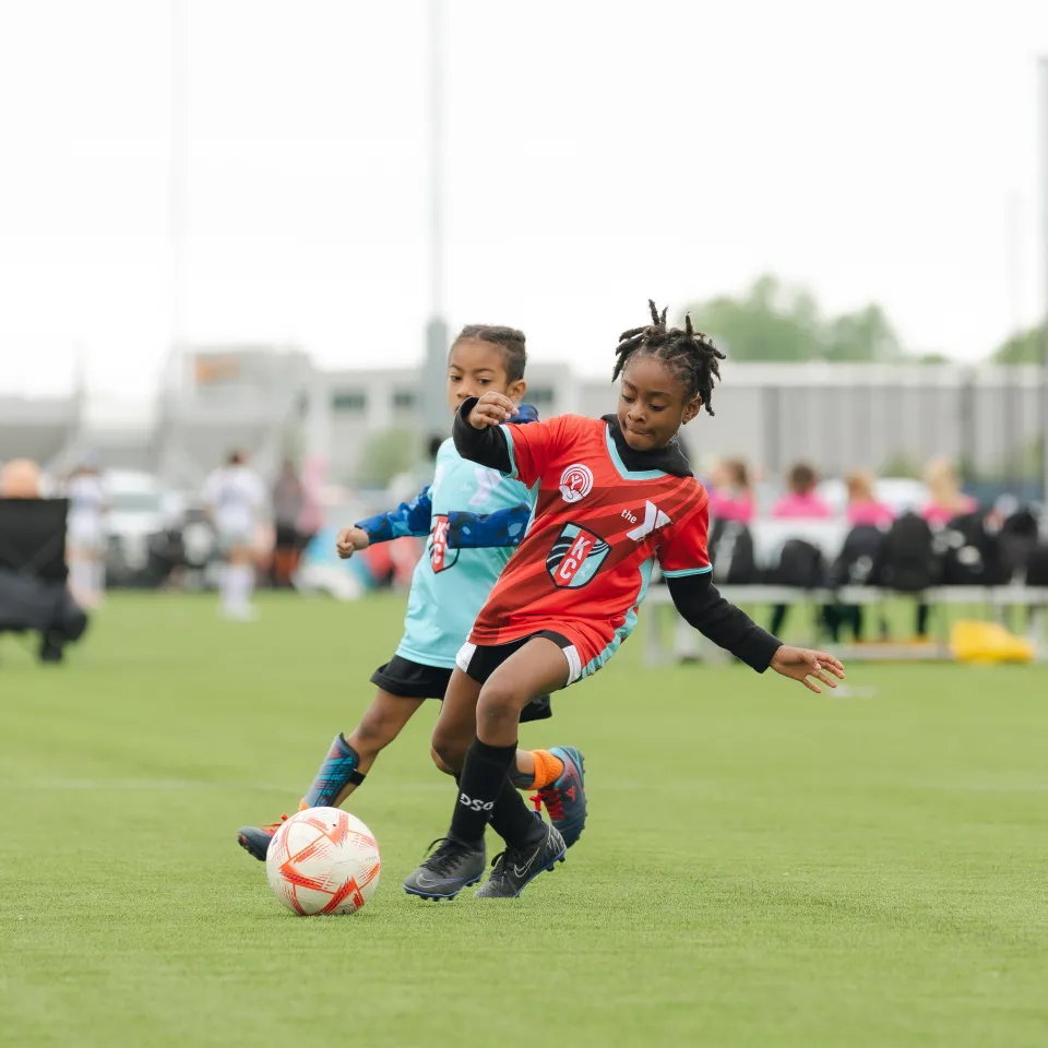 KC Current YMCA Youth Soccer player kicks ball, defender is in the background.