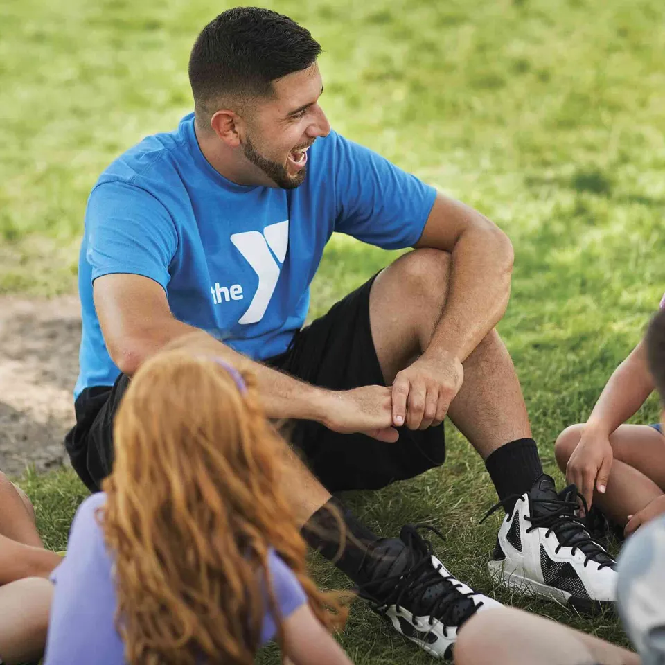 A small group of children sitting in a circle around a Y staff member enjoying the outdoors.