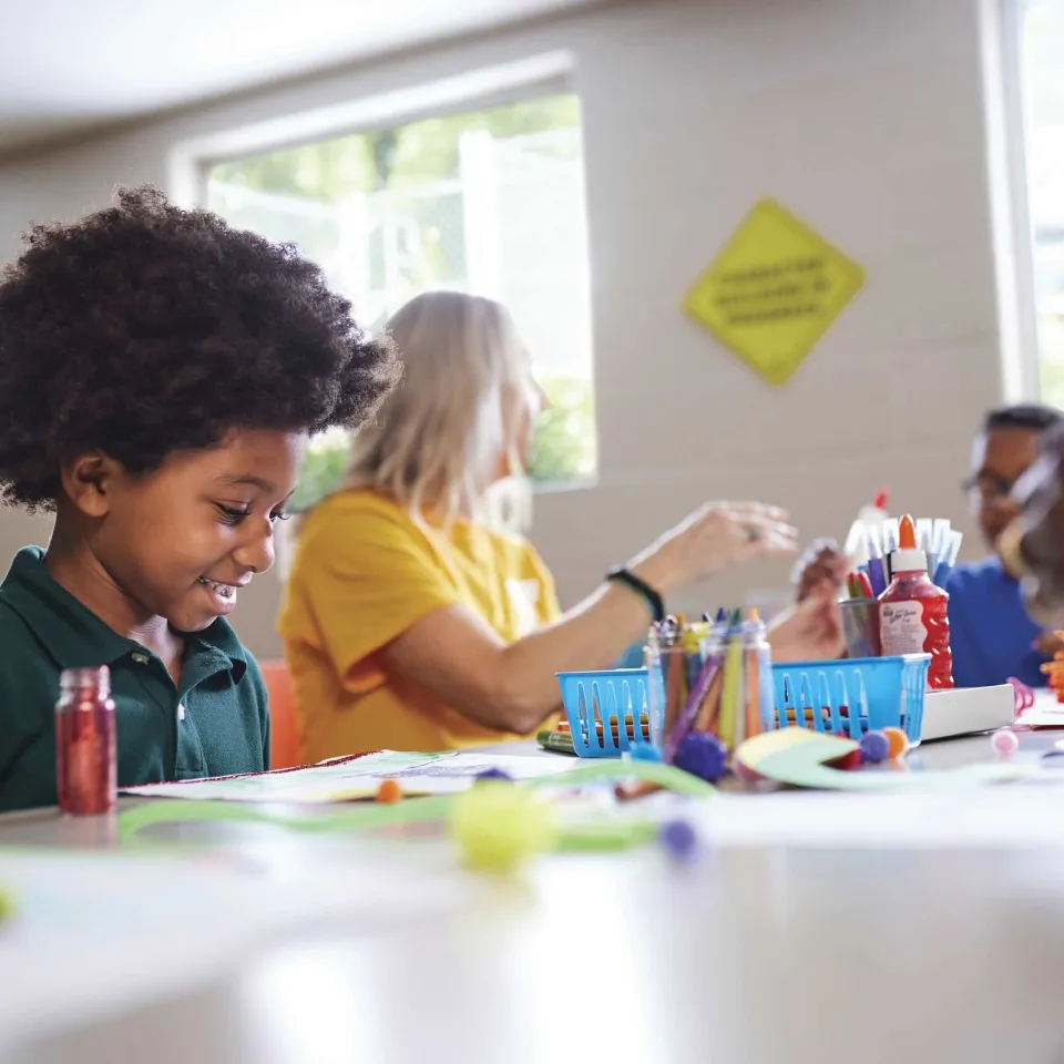 A child sits next to a Y staff member while doing arts and crafts indoors.