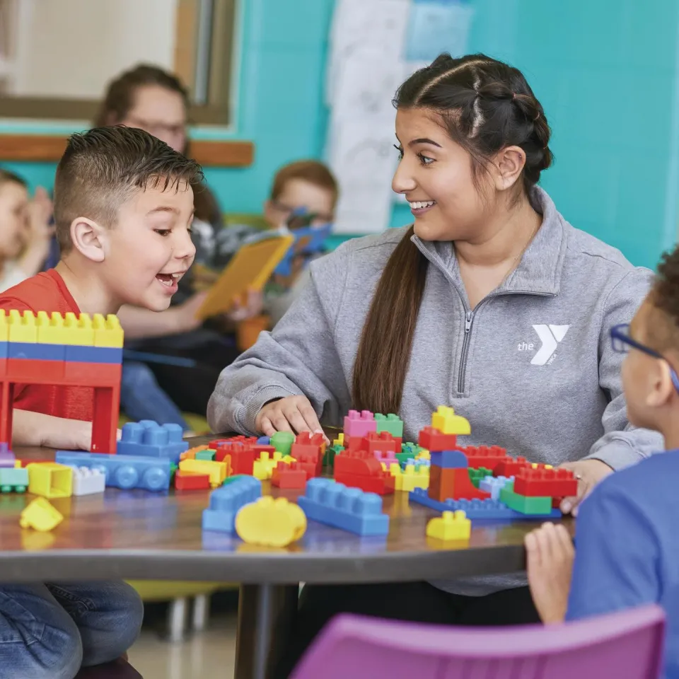 Two children play with legos at a table with a Y staff member