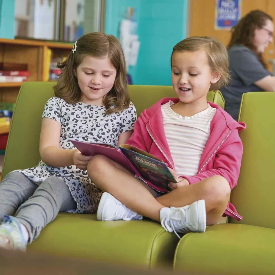 Two young girls reading together on a chair.