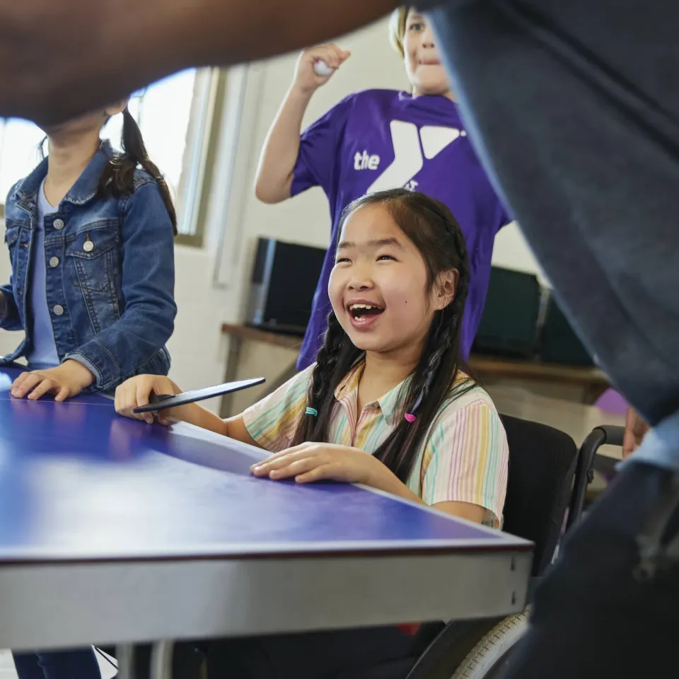 Afterschool children are laughing and playing ping pong indoors.