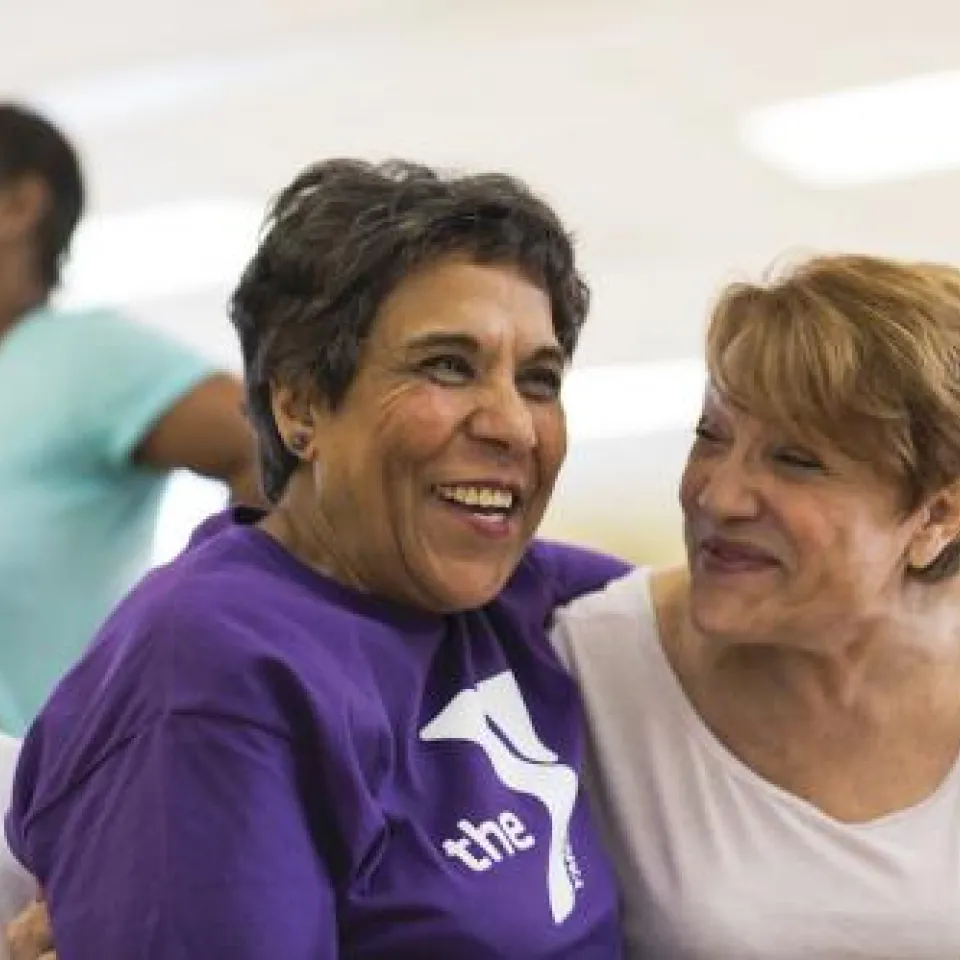 Two happy older women leaning into each other while sitting down 