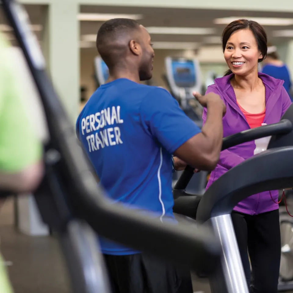 Personal trainer showcasing treadmill equipment at Kansas City YMCA gym to new YMCA member.