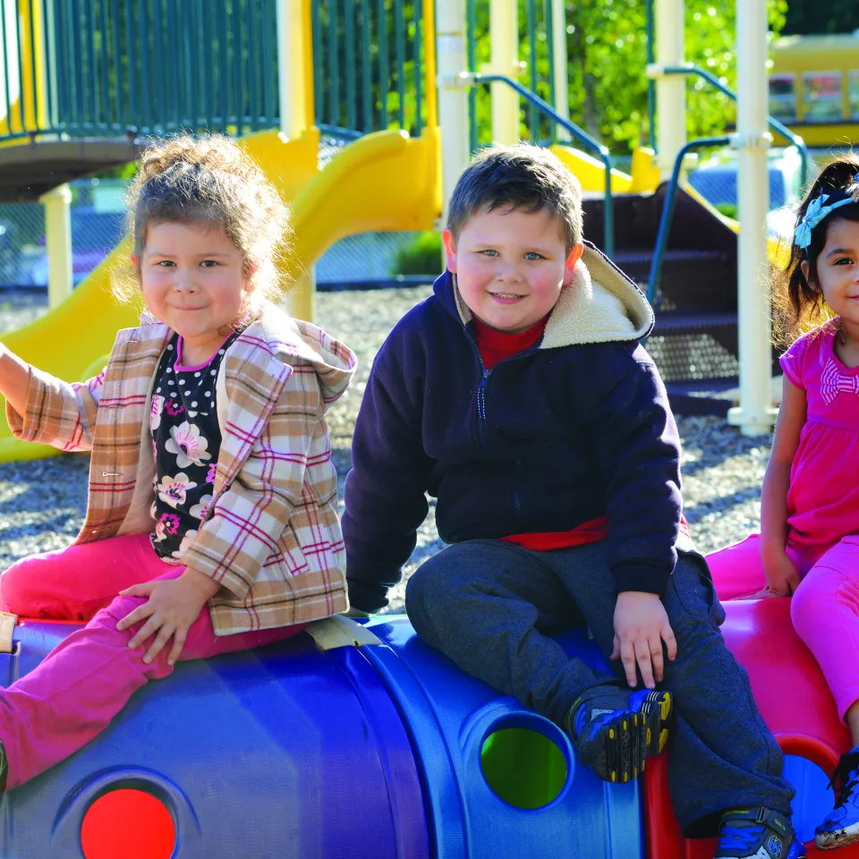 3 children sitting on plastic tunnel at Greater Kansas City YMCA playground.