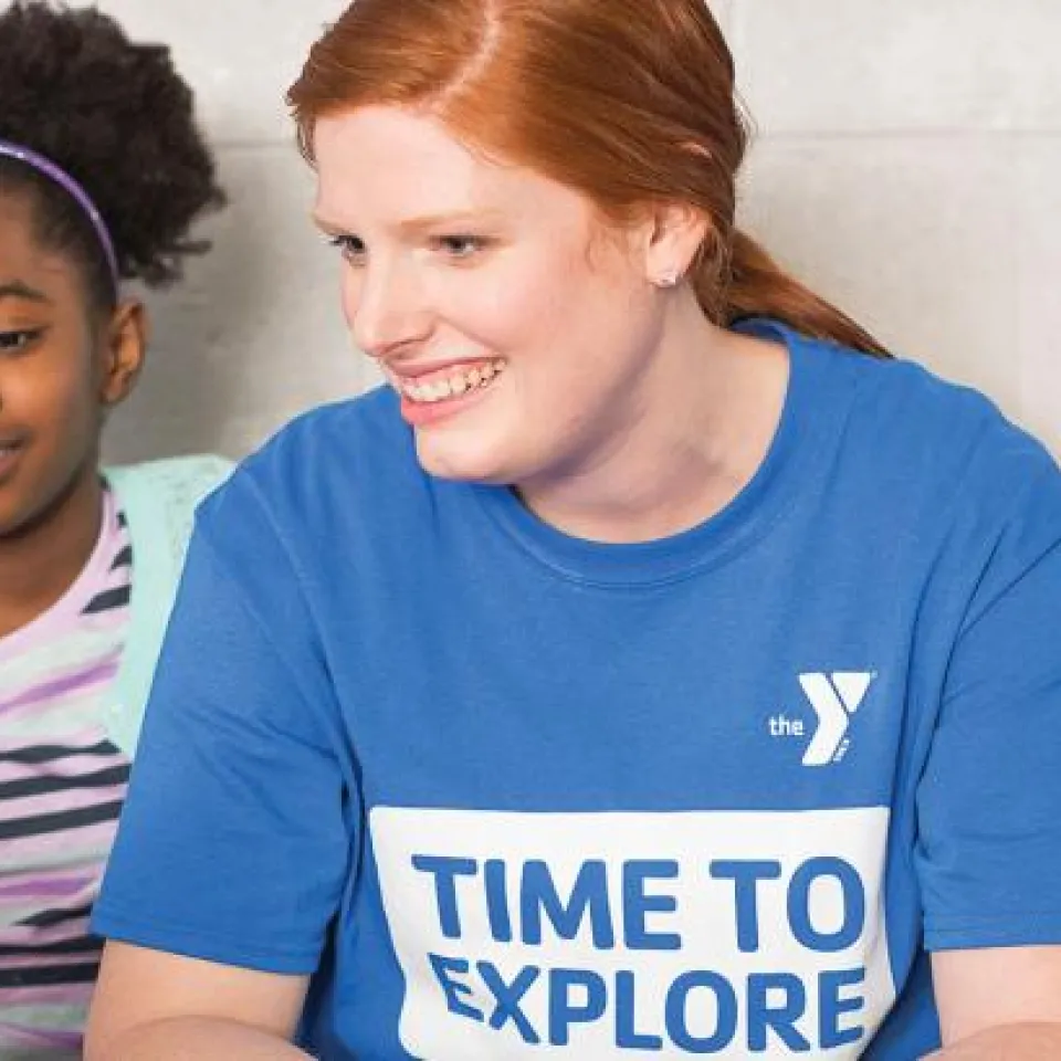 Kansas City YMCA employee assisting children while reading.