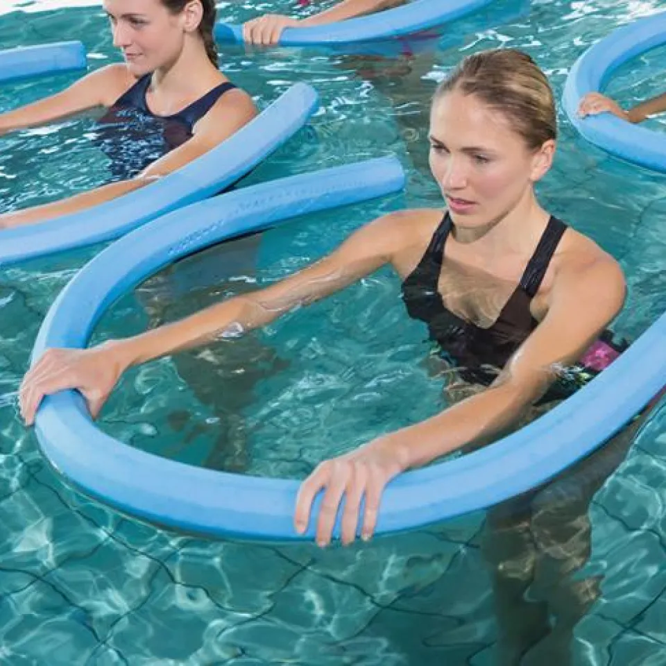 4 women hold pool noodles for stability while exercising in Greater Kansas City YMCA Water Fitness Class.