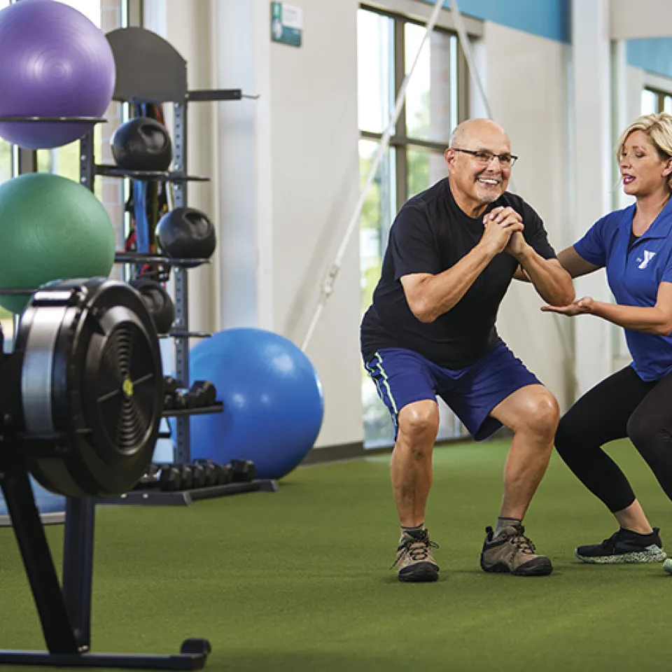 Physical trainer assists an active older adult with his workout.