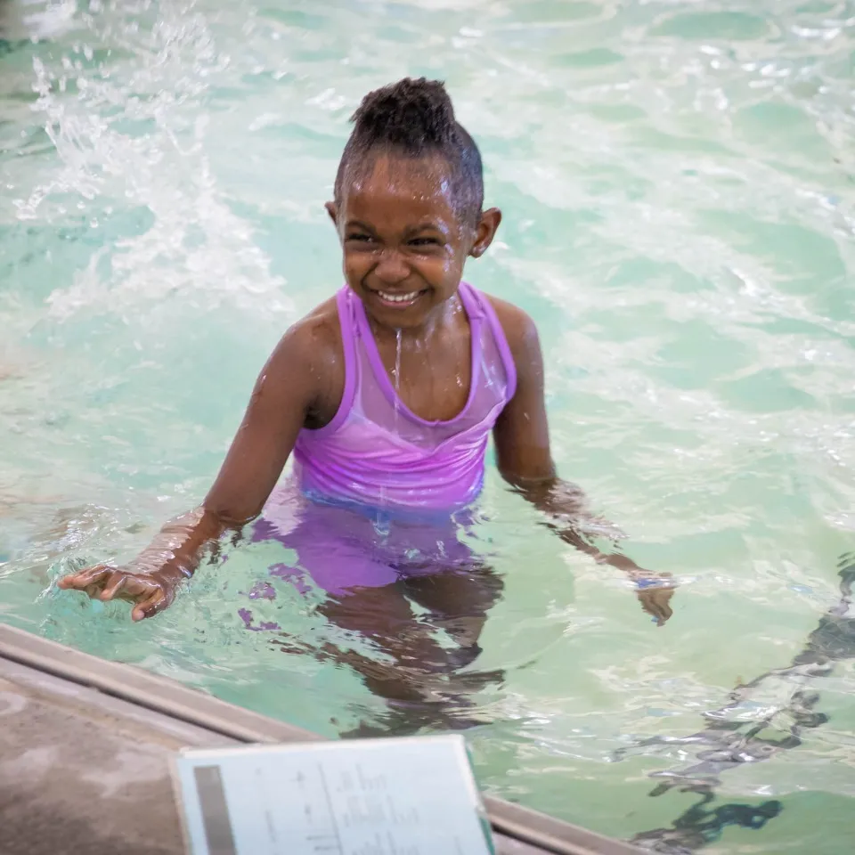 Young Providence YMCA member smiles in the pool during swim lessons.