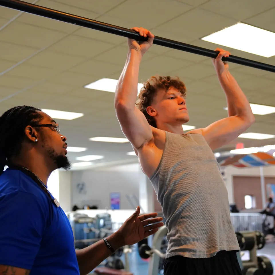 YMCA Trainer helps man do pullups on a bar at Greater Kansas City gym.