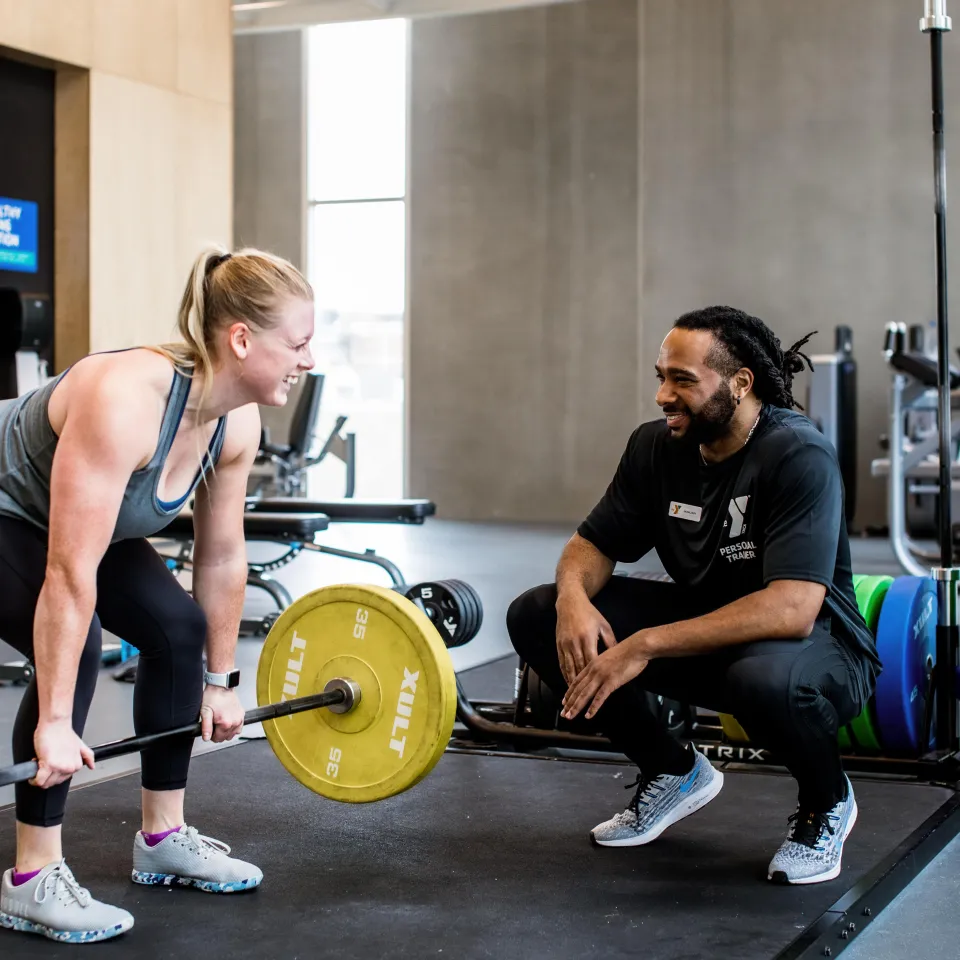 Y Personal Trainer instructing a Y Member how to lift weights. Y Member is in a bend over rowing position. 