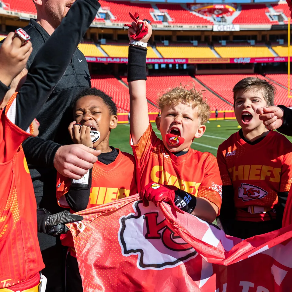 Five boys in YMCA Chiefs Flag Football uniforms cheering with arms in the air