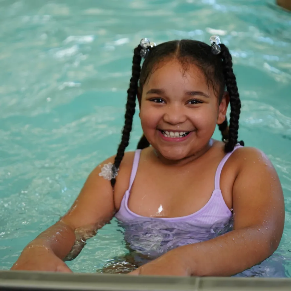 Photo of girl in pool, hands on the edge, with a big smile