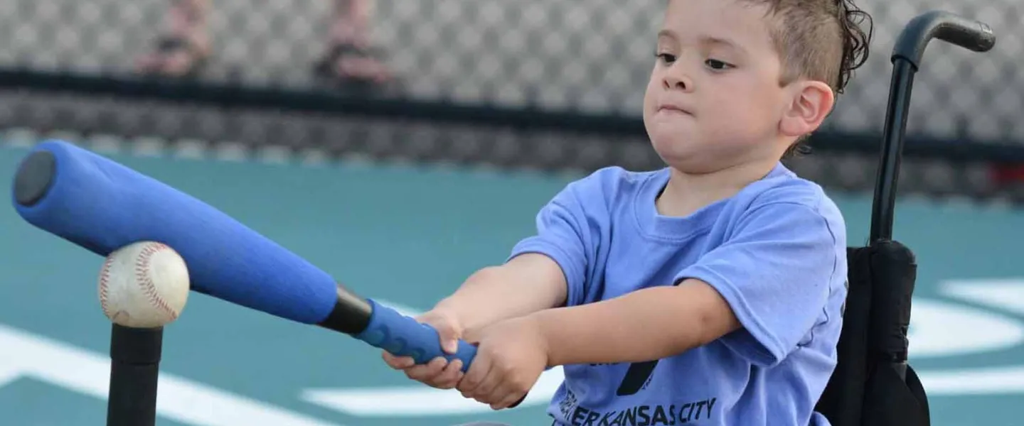 Young boy in wheelchair swings at ball on tee.