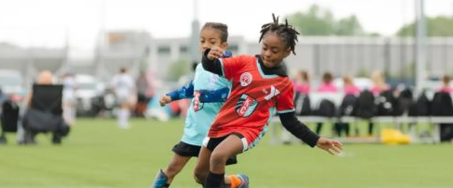 2 kids from opposing teams going after the same ball in YMCA Soccer team.