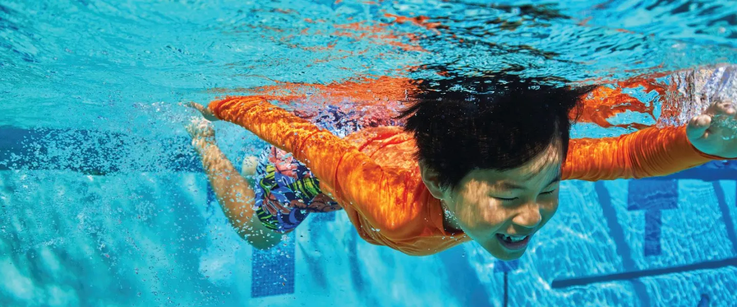Young swimmer confidently swimming with an overhand stroke at the Kansas City YMCA pool.