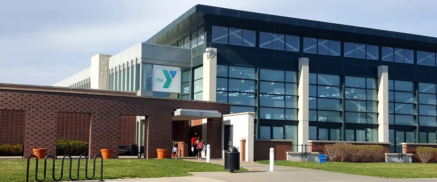 Exterior photograph of the North Kansas City YMCA. Building is made of brick on one side, floor to ceiling glass on the other, and has a bright blue YMCA logo above the entrance to the building.