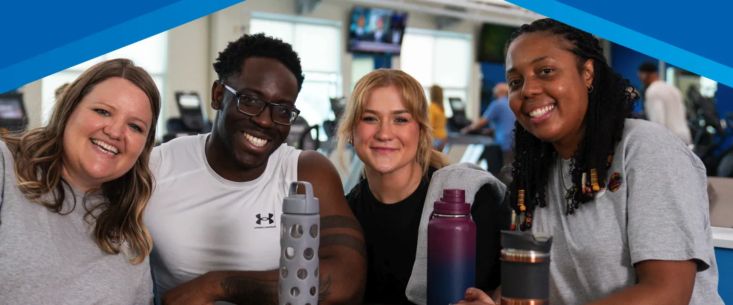 Four young adults with water bottles socialize in the lobby of the Y, smiling, after a workout
