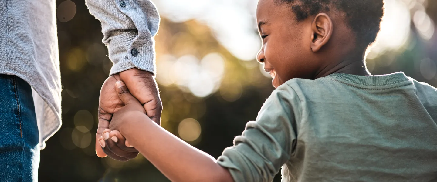 Child holding hand of an adult smiling as they walk away from the camera.