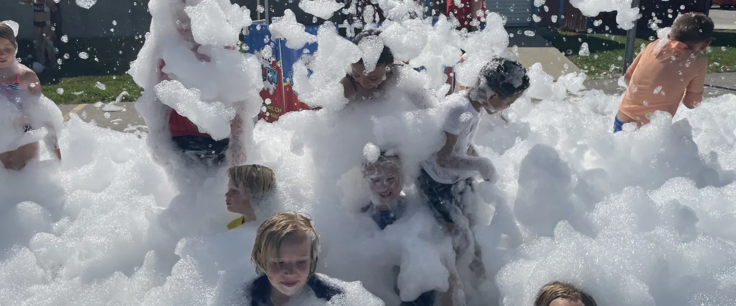 Photo of campers playing in white foam bubbles at foam party