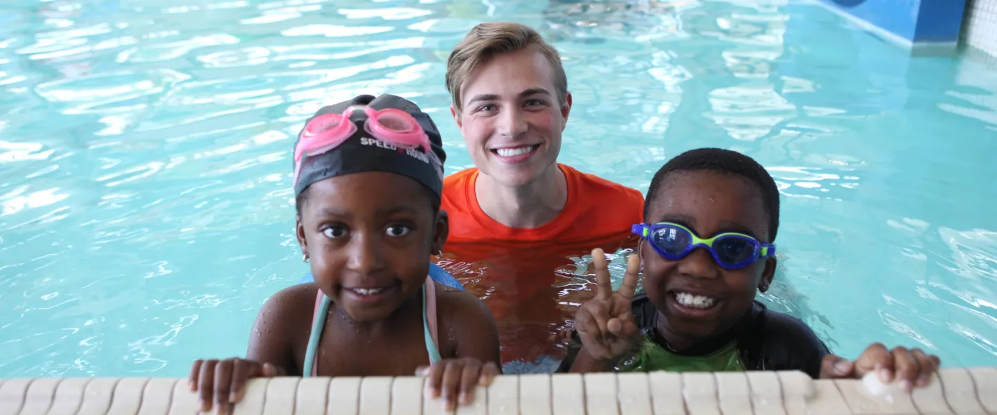 Picture of two children in the pool, pausing with their aquatic instructor.