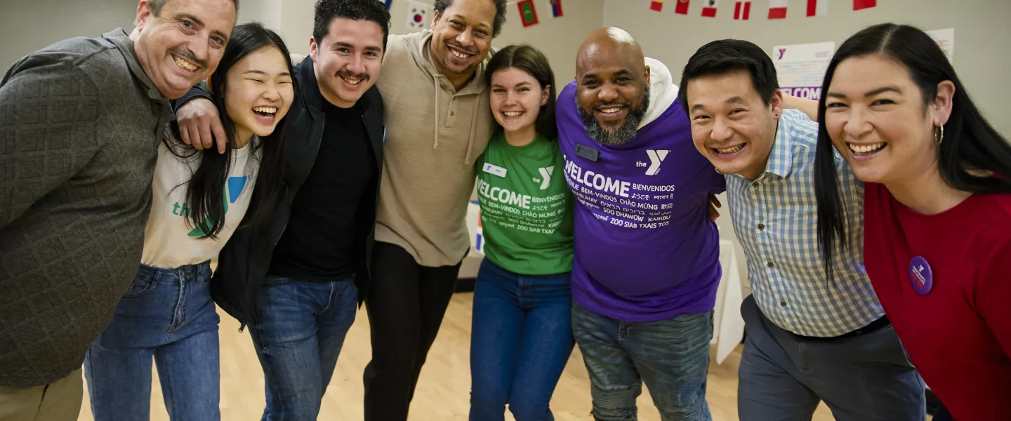 Picture of a diverse group of people joined in semi-circle, and smiling.