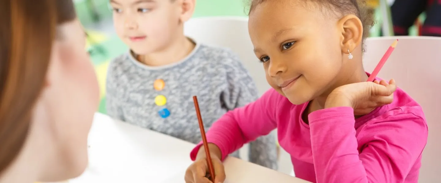 Picture of a child drawing and looking at a teacher with a smile.