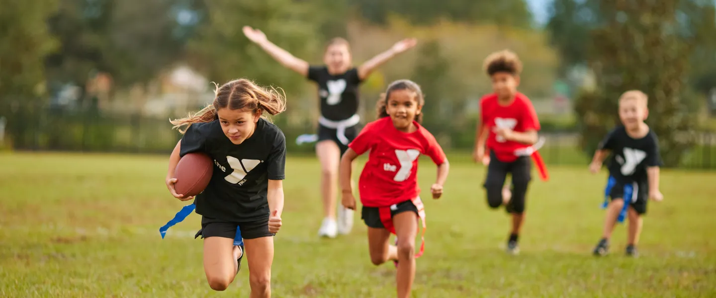 Photo of kids running toward the camera and playing flag football.