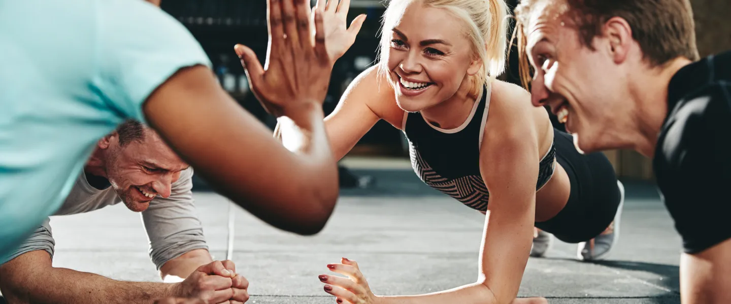 Photo of a Young woman smiling while doing planks and high-fiving workout buddy.