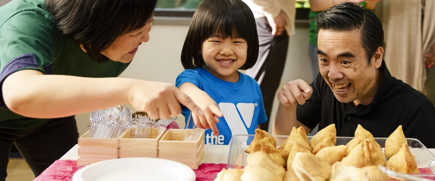 Family including young child shares food from around the world at welcoming week event