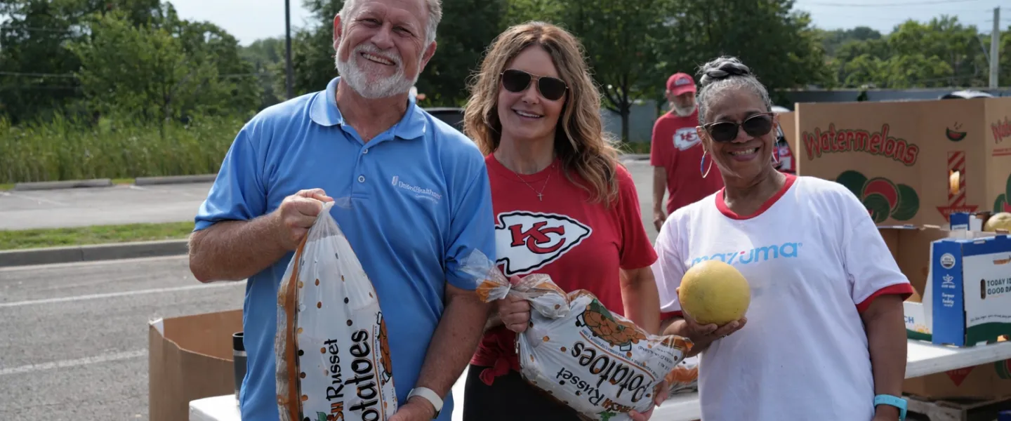 Volunteers posing with bags of potatoes and a cantaloupe while volunteering at a Cleaver food distribution events.