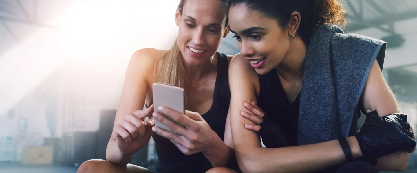 Photo of two women at the gym looking at a phone.