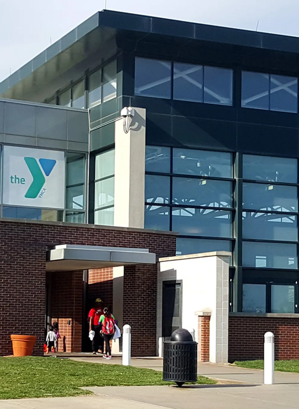 Exterior photograph of the North Kansas City YMCA. Building is made of brick on one side, floor to ceiling glass on the other, and has a bright blue YMCA logo above the entrance to the building.