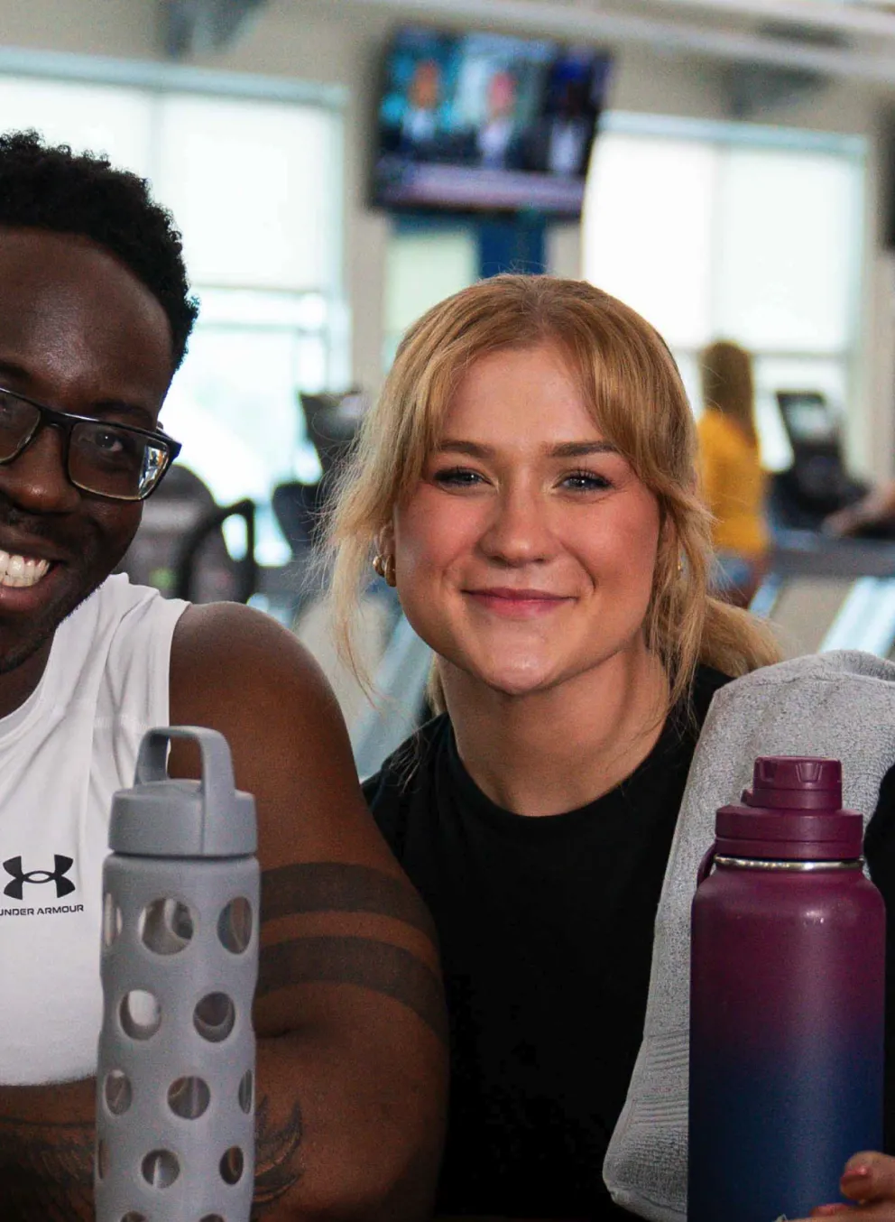Four young adults with water bottles socialize in the lobby of the Y, smiling, after a workout