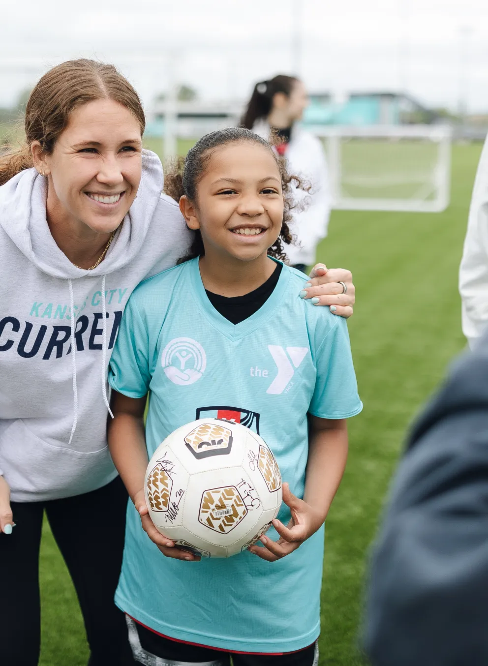 KC Current soccer player poses with girl wearing YMCA KC Current soccer jersey and holding autographed soccer ball