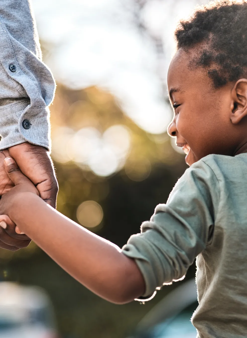 Child holding hand of an adult smiling as they walk away from the camera.