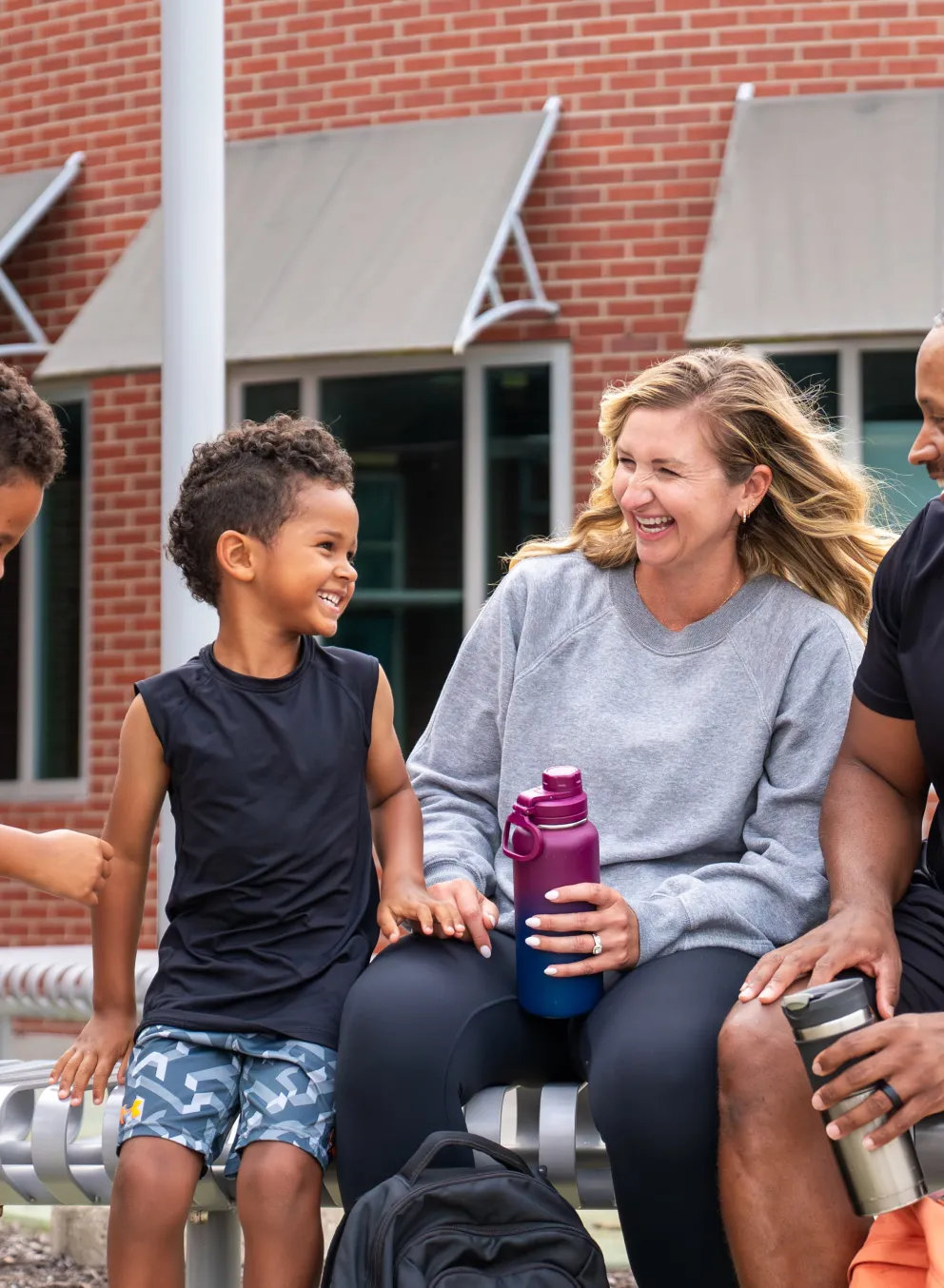 Photo of two boys, mom and dad sitting on bench outside the YMCA holding water bottles and smiling