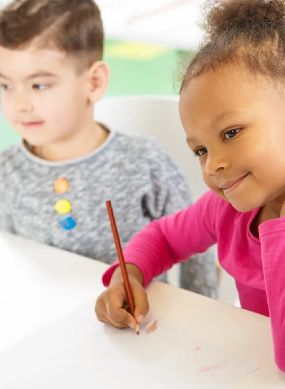 Picture of a child drawing and looking at a teacher with a smile.