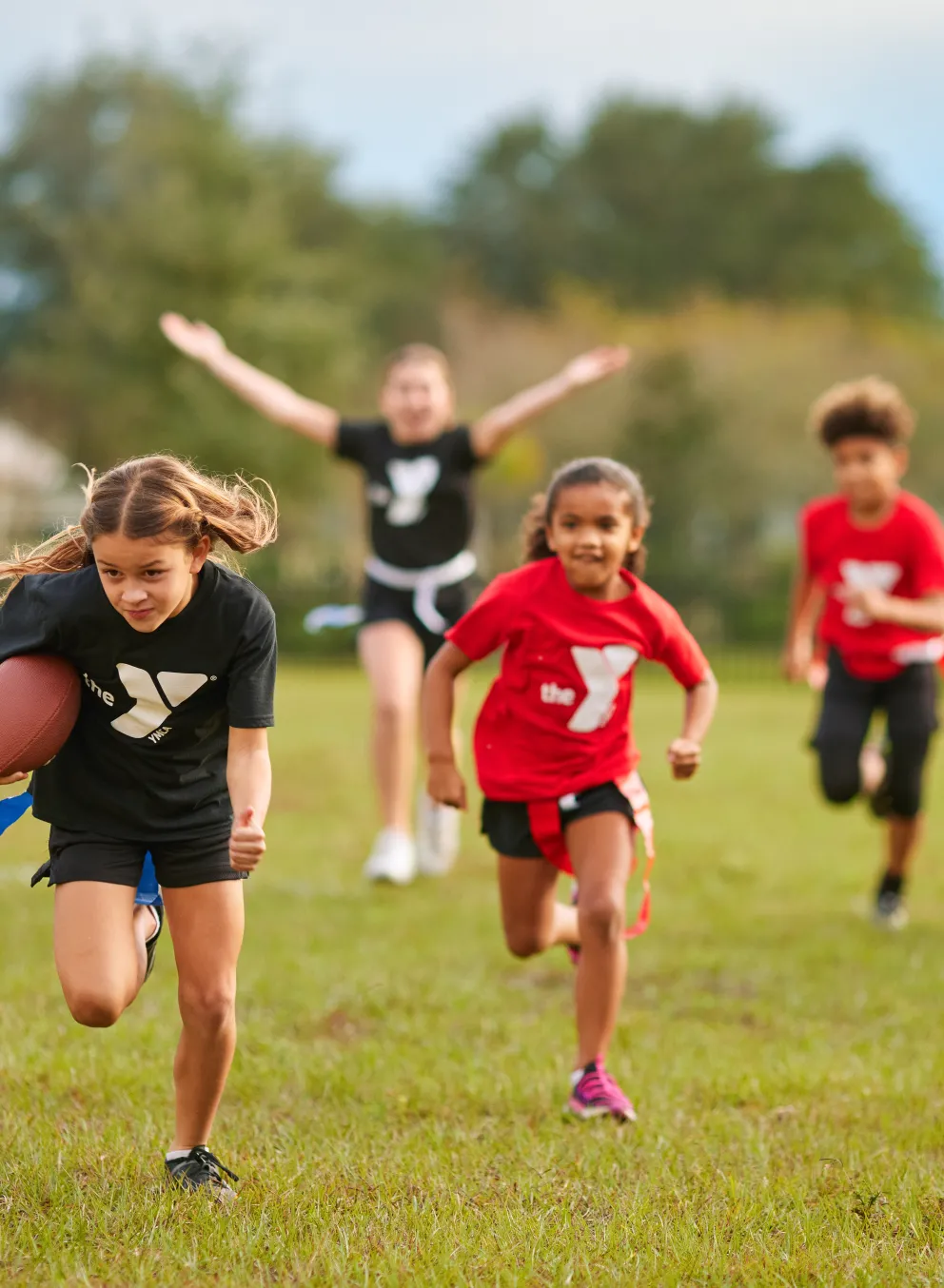 Photo of kids running toward the camera and playing flag football.