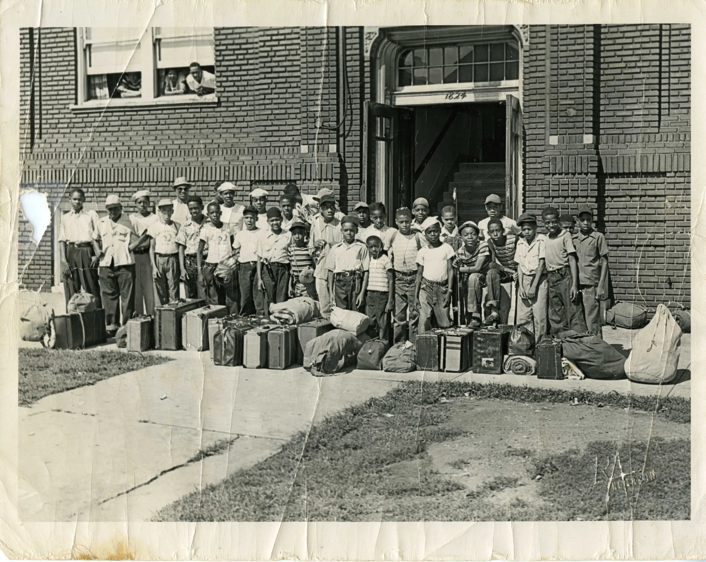 Photo from 1948 of boys outside the Paseo YMCA for summer camp with suitcases stacked in front of them