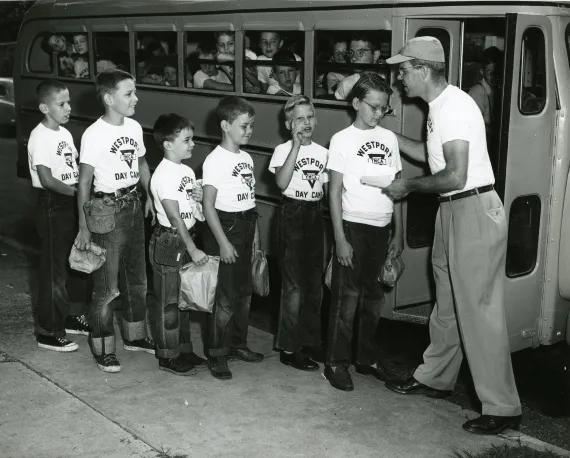 Historic photo of boys lined up to get on bus for summer day camp.
