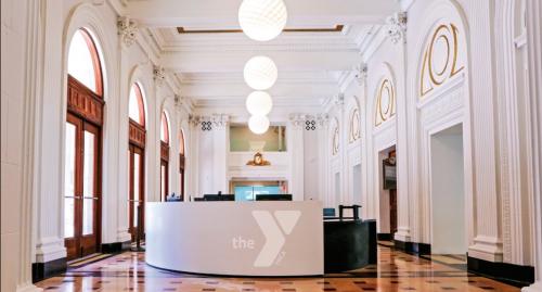 Photo of the lobby of the new Kirk Family YMCA. Shows restored lobby of the historic Lyric Theatre. In the center is the white welcome center desk with a Y logo on it.