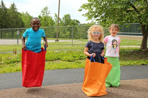 Three children in the Head Start program are jumping in jumping bags on the playground.